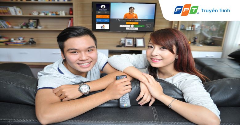 Two people with a TV behind them. The man on the left holds a TV remote.