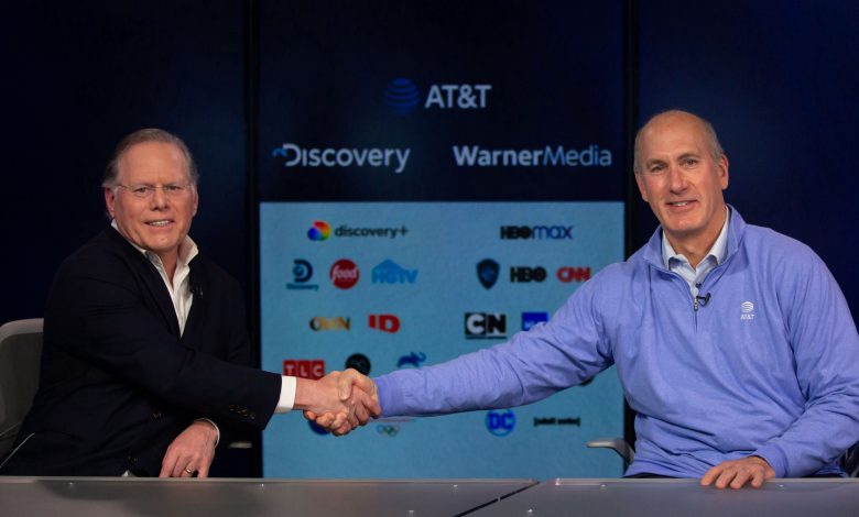Two men seated and shaking hands in the foreground, background are some logos